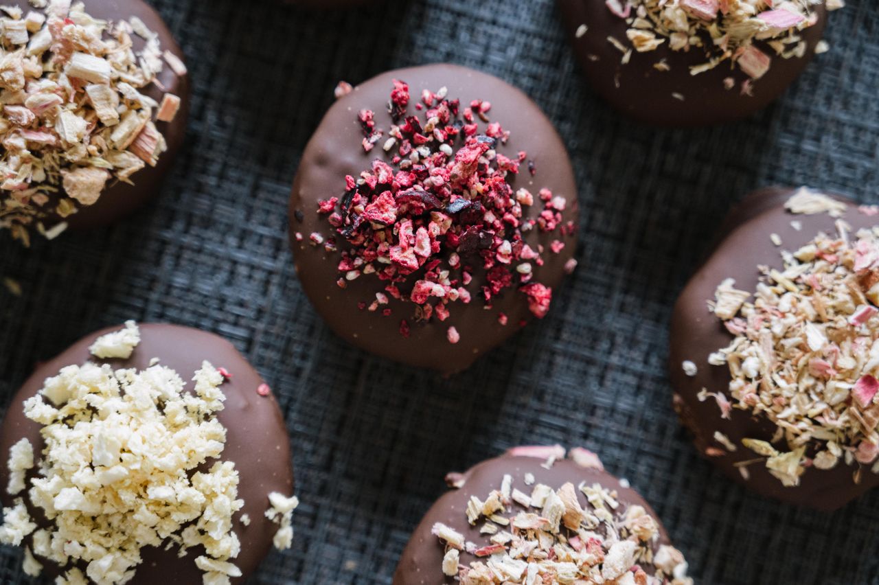A top-down view of chocolate bites topped with various dried fruits on a textured dark surface.