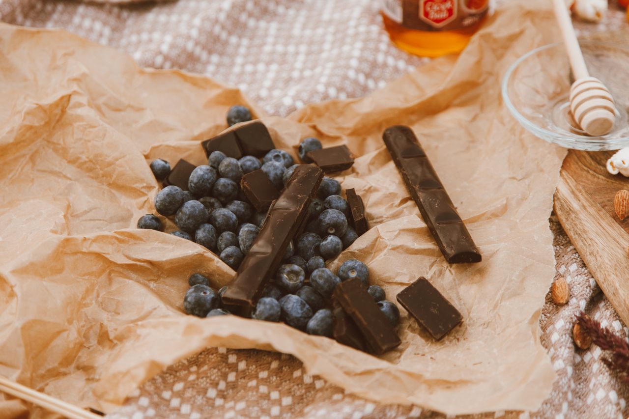 An artistic still life of blueberries and dark chocolate on parchment paper, perfect for food lovers.